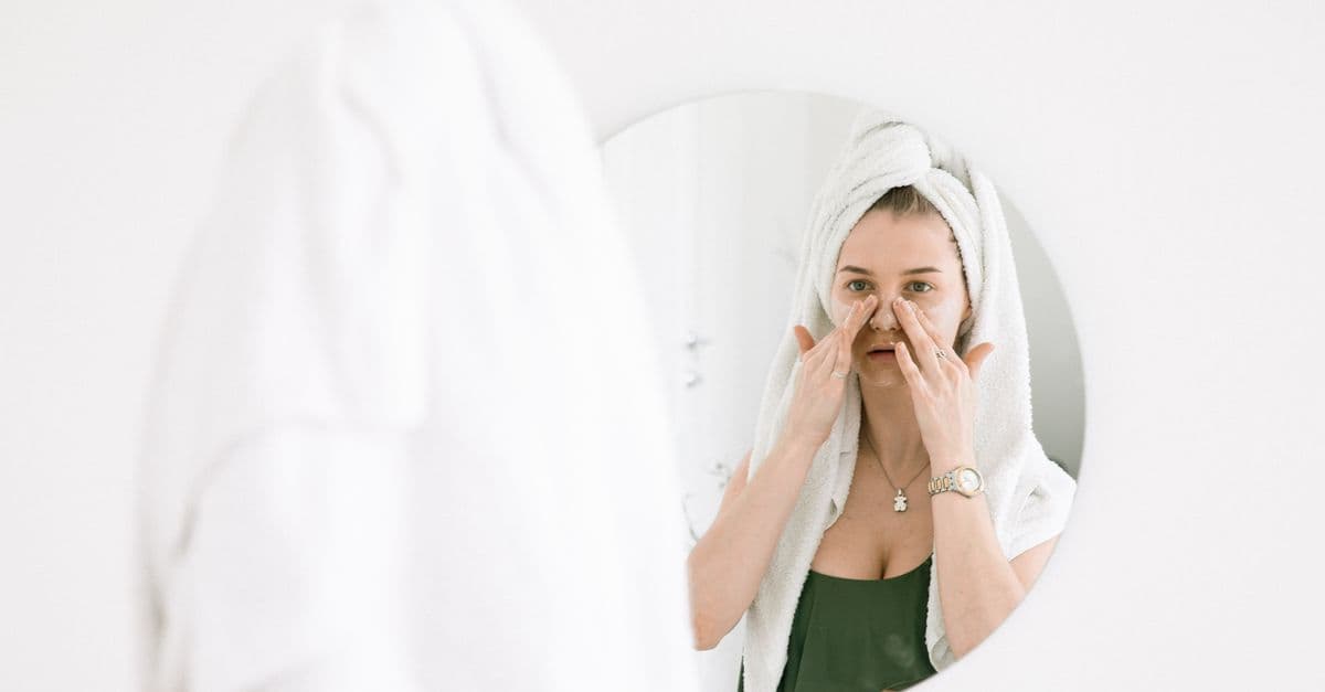 Gua sha taşıyla ayna karşısında yüz masajı yapan bir kişi